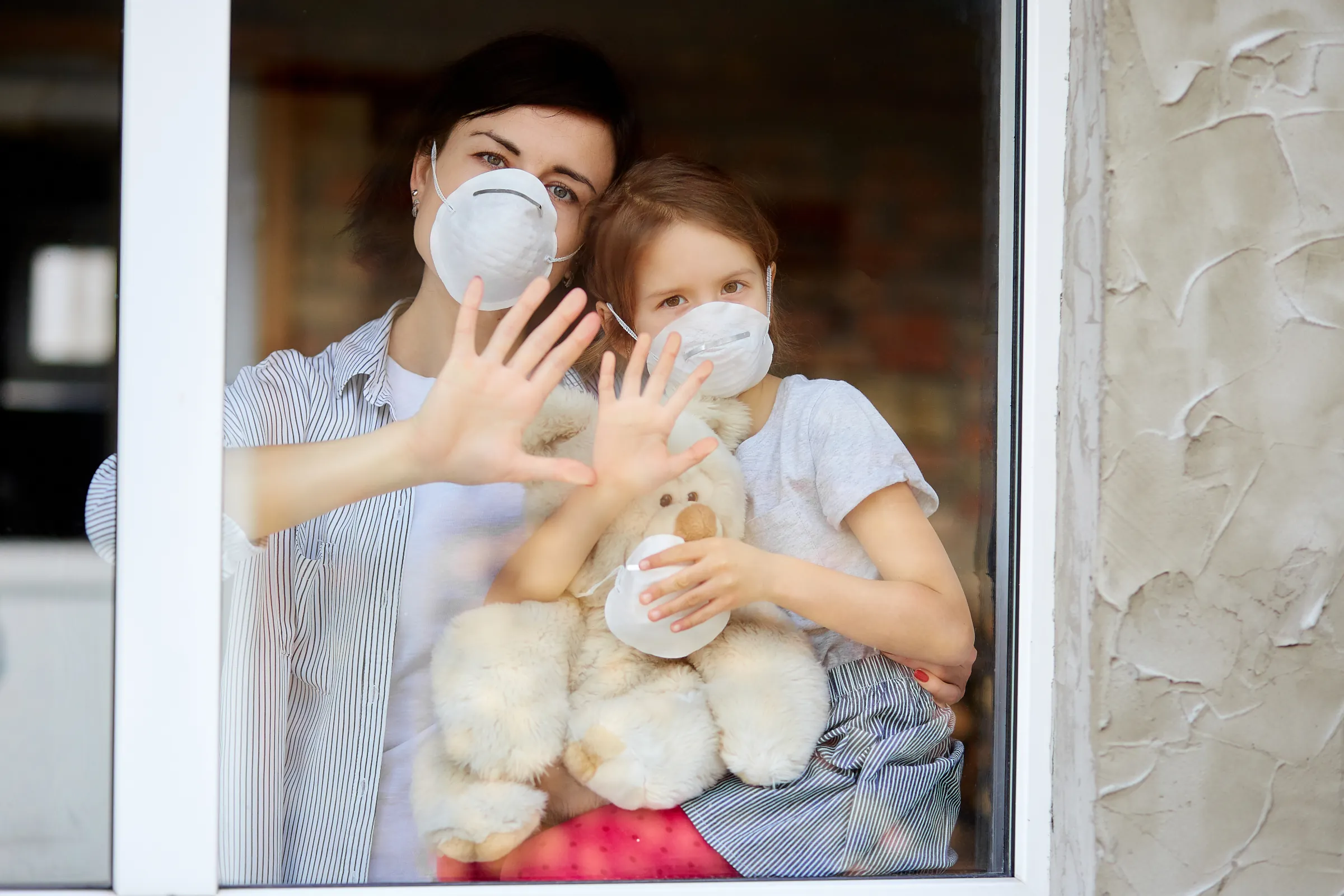 Mother with daughter child in mask looking from window, IAQ and HVAC